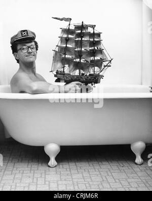 Man in captain hat holding toy ship in bathtub Stock Photo