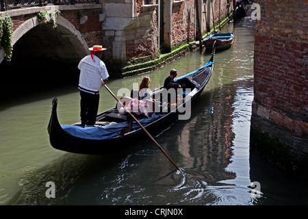 Venetian Gondolier taking passengers on a trip on a canal in dappled subdued light , Venezia Stock Photo