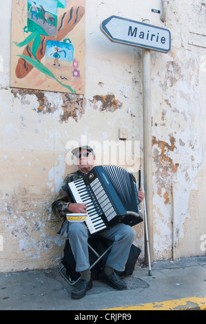 blind musician playing accordion in front of a bakery, France, Languedoc-Roussillon, Saint Gilles Stock Photo
