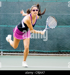 Young hispanic woman follows through on her tennis serve Stock Photo