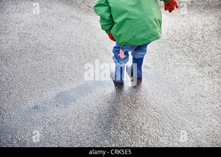 Boy in rain boots playing in puddle Stock Photo