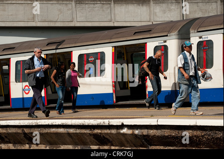 Passengers walking along a platform alongside a London Underground train at a railway station, England. Stock Photo