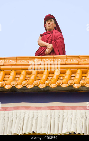 A Tibetan Buddhist monk on top of the Grand Sutra Hall in the Labrang Monastery in Xiahe chanting 'calling to prayer'. Stock Photo
