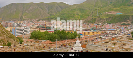 A 2 picture stitch panoramic aerial view of Xiahe town with local people circling a white stupa in the foreground. Stock Photo