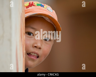 A young Tibetan Chinese boy playing peek-a-boo around a corner at the camera. Stock Photo