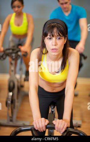 Three people cycling in a gym or fitness club, dressed in colorful ...