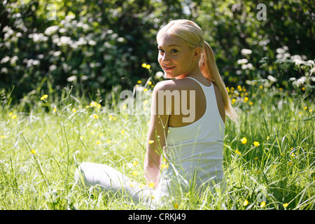 A young woman sitting amongst spring flowers, smiling Stock Photo