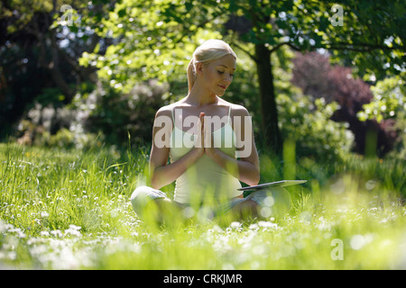 A young woman looking at a digital tablet whilst practicing yoga outside Stock Photo