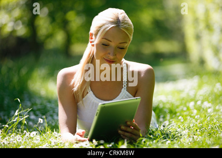 A young woman laying in the grass looking at a digital tablet Stock Photo