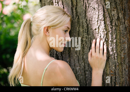 A young blonde woman leaning against a tree trunk Stock Photo