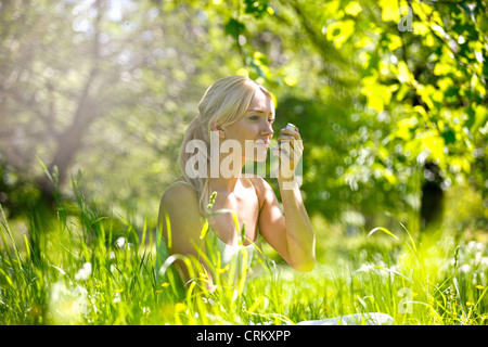 A young blond woman sitting in the grass using a asthma inhaler Stock Photo