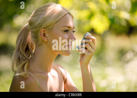 A young blond woman sitting in the grass using a asthma inhaler Stock Photo