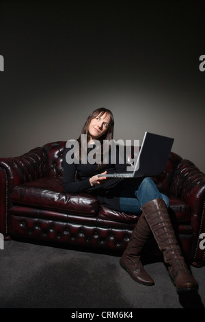 Thoughtful young woman using laptop on a couch Stock Photo