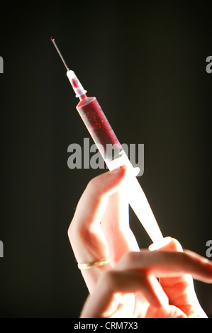 A disposable hypodermic syringe containing red fluid being held against a black background. Stock Photo