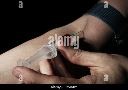 A heroin user injecting heroin into his arm. Heroin (diacetyl morphine) induces a psychological state of indifference immediately after it is taken. Repeated use causes a physical dependence and tolerance. Tolerance leads to ever-increasing doses being taken to achieve the same effect, often resulting in a fatal overdose. The withdrawal symptoms for a person Stock Photo