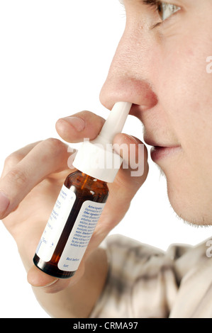 Young man using a nasal spray. Nasal spray is ideal for the relief of nasal congestion. Nasal congestion occurs when the membrane that lines the nose swells and an accumulation of thick mucus is present. Such congestion occurs when the sufferer has hay fever, sinusitis, common cold and other such allergies. Stock Photo