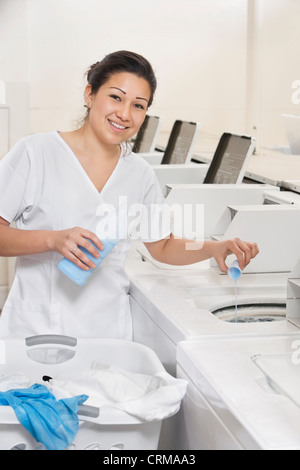 Portrait of a happy woman employee pouring detergent in washer Stock Photo