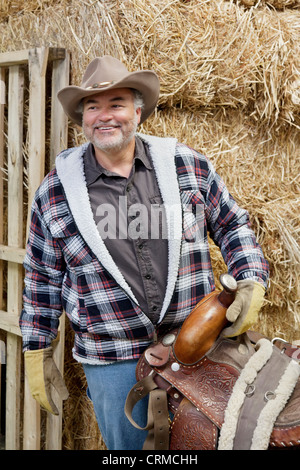 Happy mature cowboy holding saddle Stock Photo