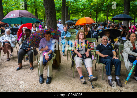 Paris, France, French Audience, Large crowd People, diverse Audience in Rain With Umbrellas Listening to National Music Festival, 'Fete de la Musique', Classical Music Concert in Luxembourg Gardens, sitting down Stock Photo