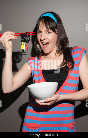 Cheerful young woman with electric cable rolled up as noodles on chopsticks Stock Photo