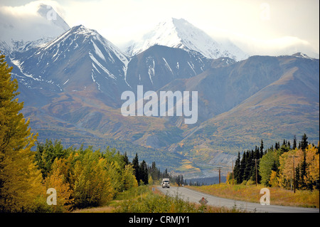 Eighteen wheeler or truck driving on a highway through snow-capped mountains and autumn or fall colours in Yukon, Canada Stock Photo