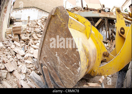 Side view of yellow digger demolishing a building and clearing the rubble, illustrating the construction sector in ruins, Spain Stock Photo