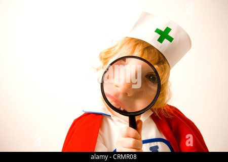 Young girl dressed as a nurse looks through a magnifying glass Stock Photo