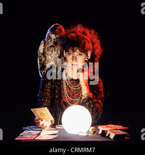 Gipsy fortune teller with an owl on her shoulder, tarot cards and lit crystal ball Stock Photo