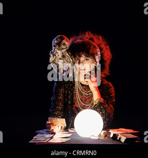 Gipsy fortune teller with an owl on her shoulder, tarot cards and lit crystal ball Stock Photo