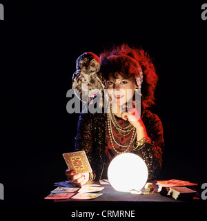 Gipsy fortune teller with an owl on her shoulder, tarot cards and lit crystal ball Stock Photo