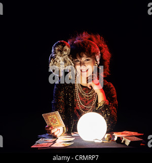 Gipsy fortune teller with an owl on her shoulder, tarot cards and lit crystal ball Stock Photo