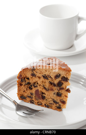 Slice of rich fruit cake with dessert fork with cup and saucer in background Stock Photo