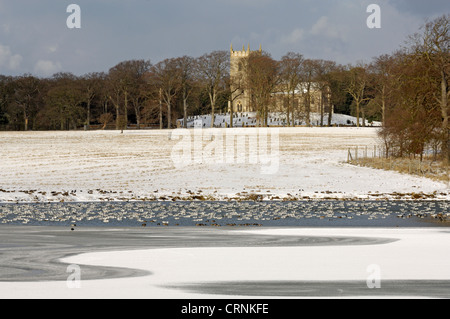 Winter view over a frozen lake towards St Withburga church in the grounds of Holkham hall. Stock Photo