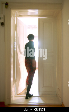 Woman opens door to a brightly lit room Stock Photo