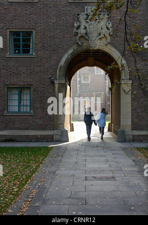 A couple walking hand in hand through an archway in the grounds of Trinity College. Stock Photo