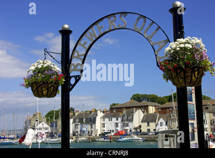Baskets of flowers hanging by a sign at the entrance into Brewers Quay in the seaside resort of Weymouth. Stock Photo