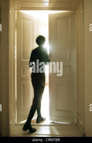 Woman opens door to a brightly lit room Stock Photo