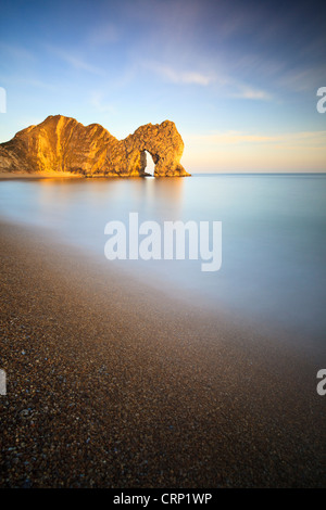 The sun casts warm light onto Durdle Door, a natural Limestone arch near Lulworth Cove, part of the UNESCO Jurassic Coast. Stock Photo