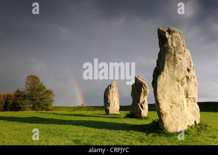 Standing stones, part of the Avebury ring, with the end of a rainbow falling on two people in the background. Stock Photo