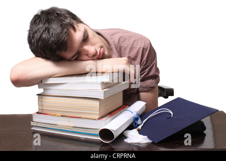 Male student sleeping on textbooks with graduation certificate and blue cap on a wooden desk Stock Photo