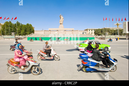 With motion blur.  Vehicles and people travel past the statue of Mao Zedong opposite the city square in Kashgar. Stock Photo