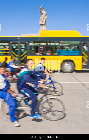 With motion blur.  Young Chinese school boys on bicycles travel past the statue of Mao Zedong in Kashgar.