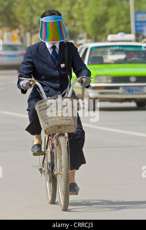 A Chinese woman travels along a road on her bicycle in Kashgar wearing a sun shield visor. Stock Photo