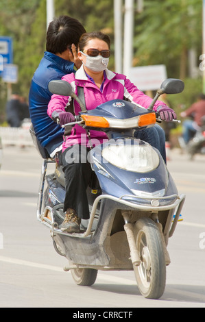 A Chinese couple travel along a road on their scooter in Kashgar with the passenger talking on a mobile phone. Stock Photo