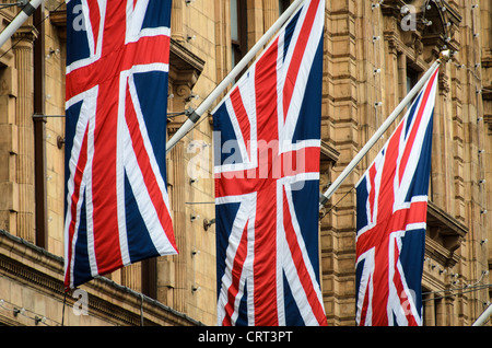 Harrods Knightsbridge Union Jack Flags London | LONDON, United Kingdom — Three Union Jack flags hang against the terracotta facade of Harrods in Knightsbridge, the ornate Edwardian cladding visible behind them. Founded as a grocery by Charles Henry Harrod in 1849, the store moved into its current terracotta building in the early 1900s and displays the flags as a permanent emblem of its identity as one of Britain's best-known luxury department stores. Stock Photo