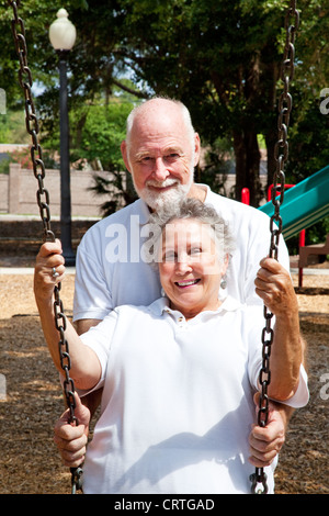 Romantic senior husband pushing his lovely wife in a swing on a playground.  Stock Photo