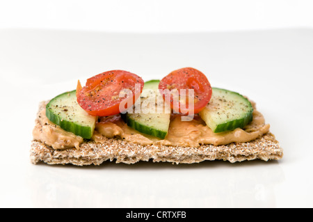 Crisp breads with peanut butter, sliced cucumber and tomato on white plate with seasoning on top Stock Photo