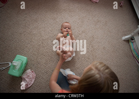 Older sister changing diaper for ten month old sister at home. Stock Photo
