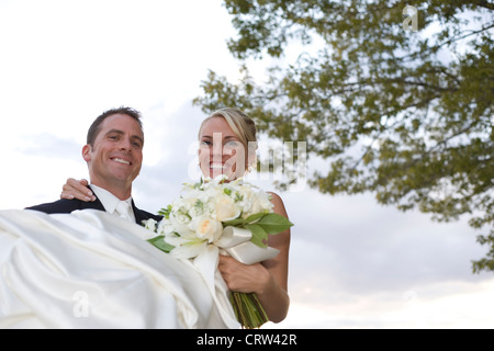 Groom holds bride outdoors just after wedding ceremony. Stock Photo