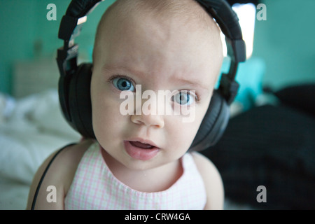 One year old girl wearing large headphones and looking wide-eyed. Stock Photo